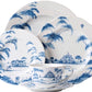 The Juliska Country Estate Delft Blue Dinnerware Collection features four white porcelain dishes and a teacup adorned with blue pastoral scenes of trees, houses, a horse stable, and a hot air balloon for countryside charm.