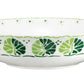 The Cobblers Cove Calypso Dinnerware Collection by Royal Crown Derby features a shallow white ceramic bowl adorned with vibrant green leaf patterns, creating a fresh Caribbean ambiance.