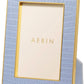 The Aerin Classic Croc Leather Frame Collection features a rectangular photo frame with light blue Italian croc-embossed leather, gold trim, and an upright stand. A card labeled "AERIN" is displayed in the empty space.