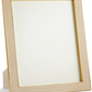The Classic Croc Leather Frame Collection by Aerin features a beige textured photo frame with gold edges, crafted from Italian croc-embossed leather and displayed at an angle with a blank insert.