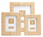Three distinct-sized frames from the Two's Company Criss Cross Weave Frame Collection are arranged in a staggered formation against a white backdrop. Each frame, designed by Two's Company, boasts a natural rattan Criss Cross weave and includes a placeholder card adorned with a gold "T" logo in the center. These frames are perfect for adding charm to your tabletop display.