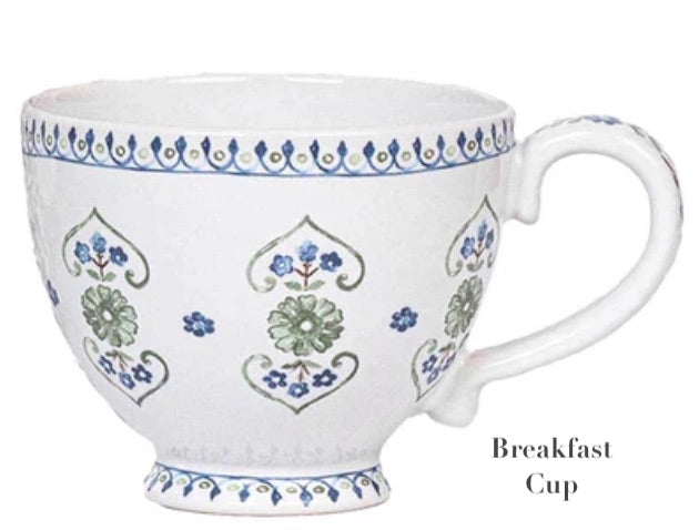 The Juliska Villa Seville Chambray Breakfast Cup features white ceramic with blue and green floral motifs, a handle, and a blue rim and base—an elegant piece from the Villa Seville Chambray Dinnerware Collection.