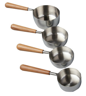 The Be Home Stainless Steel and Teak Measuring Cup Set features four cups with handcrafted teak handles, displayed in a row on a white background.