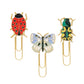 Three gold paperclips with enamel toppers—a red ladybug, a blue butterfly, and a green-yellow beetle—bring the Curio Desk Accessory Collection by Riffle Paper Co. to life, perfect for garden lovers.