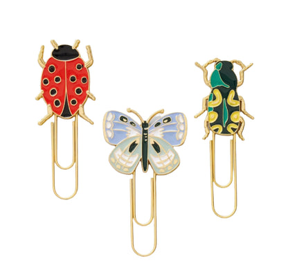 Three gold paperclips with enamel toppers—a red ladybug, a blue butterfly, and a green-yellow beetle—bring the Curio Desk Accessory Collection by Riffle Paper Co. to life, perfect for garden lovers.