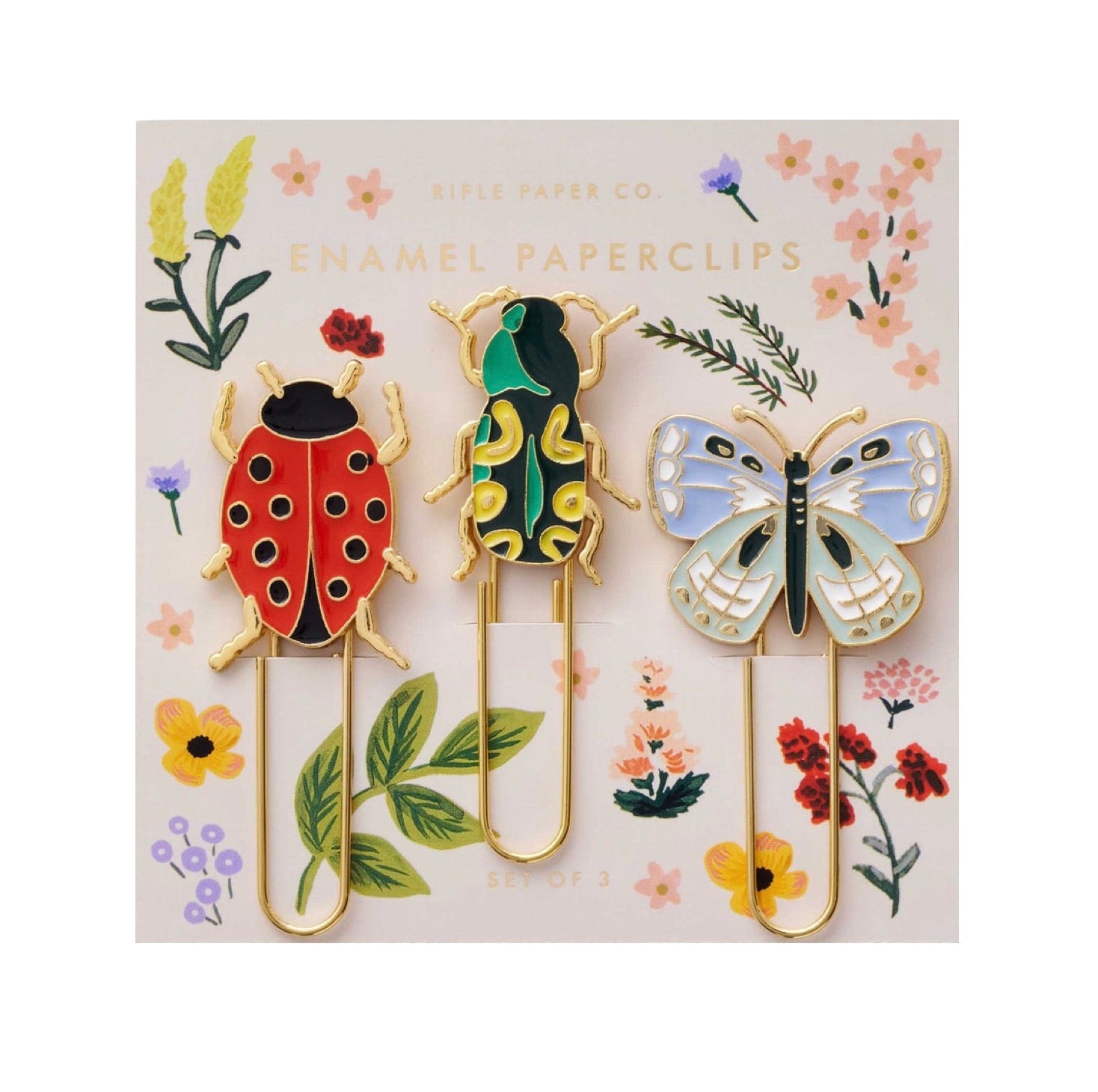 Three enamel paperclips—a ladybug, beetle, and butterfly—are displayed on a floral Riffle Paper Co. backing card from the Curio Desk Accessory Collection, making a whimsical gift or desk addition for garden lovers.