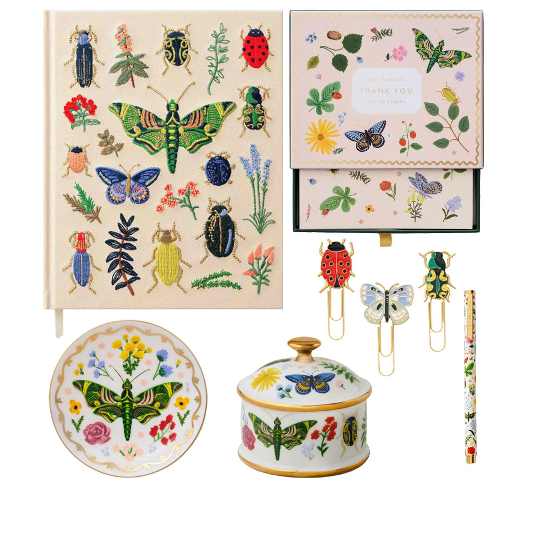 The Curio Desk Accessory Collection by Riffle Paper Co. features a notebook, greeting cards, paper clips, plate, lidded jar, and pen with vibrant bug and plant illustrations—ideal for garden lovers.