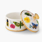 A porcelain box from the Curio Desk Accessory Collection by Rifle Paper Co., with a gold-rimmed lid ajar, features vibrant floral designs and whimsical bugs—a charming addition for garden enthusiasts.