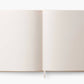 An open blank book from the Curio Desk Accessory Collection by Riffle Paper Co., featuring cream pages and a ribbon bookmark—ideal for garden lovers to sketch bugs or record discoveries.