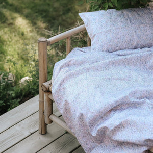 The Gooselings Enchanted Wildflowers Toddler Duvet is styled on a wooden outdoor bed with patterned bedding, set on a deck beside lush green grass and foliage.