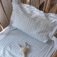 A crib with Gooselings’ Picnic Gingham Blue Toddler Pillow, a blue and white gingham bedding set, plus a small white stuffed bunny for sweet dreams.