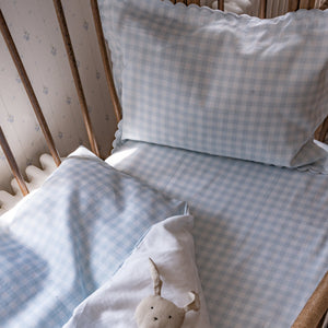 The Gooselings Picnic Gingham Blue Toddler Duvet, with its light blue and white checks, plus a matching pillow and soft rabbit toy on a white blanket, creates a cozy space—perfect before transitioning to a big-kid bed.