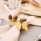A beige napkin from Juliska's Forest Walk Tabletop Collection is held by a gold ring with leaf and acorn accents, adding elegant oak-inspired decor to the dining table.