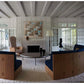 A living room from Transformation: Houses, Places, Stories, blending classical tradition with modern living, with two curved blue sofas, a coffee table, and a fireplace with textured artwork above.