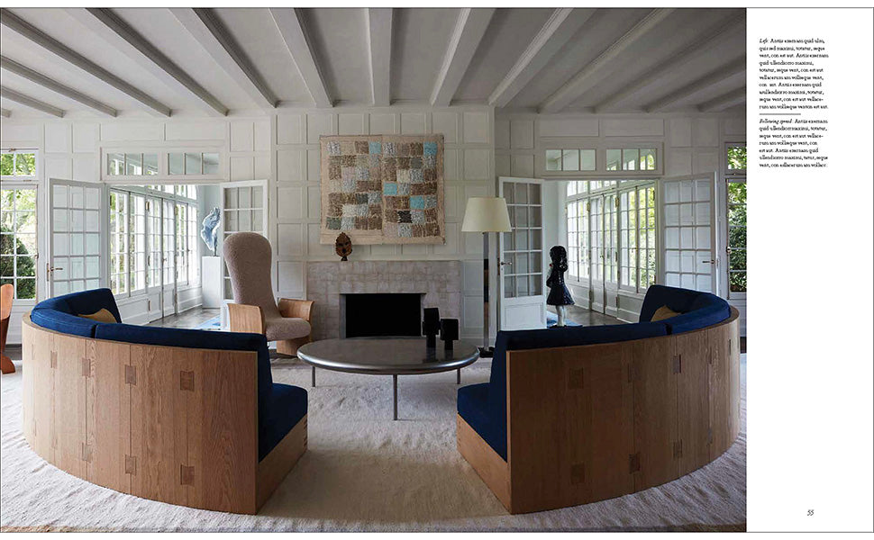 A living room from Transformation: Houses, Places, Stories, blending classical tradition with modern living, with two curved blue sofas, a coffee table, and a fireplace with textured artwork above.
