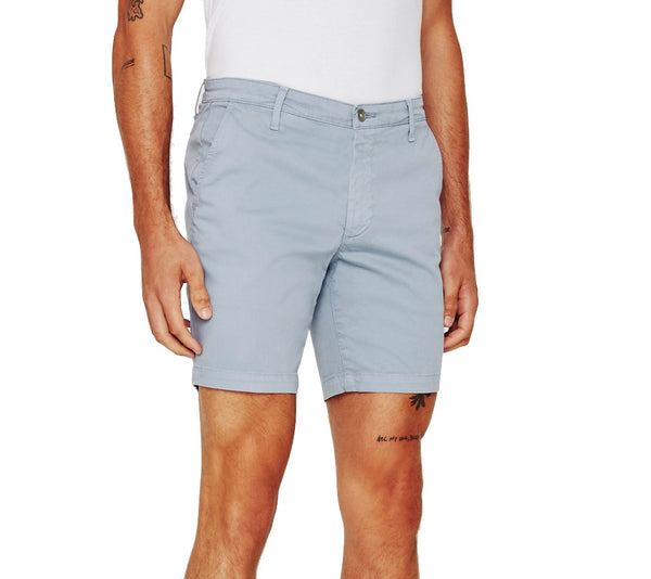 Man wearing light blue AG Jeans Wanderer Short slim fit men's shorts standing with hands on his thighs, showing a small tattoo on his left leg.