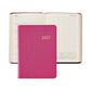 A pink Graphic Image 2027 Daily Journal closed, positioned in front of an open appointment book that displays a week in July and small yearly calendars at the bottom of the pages.