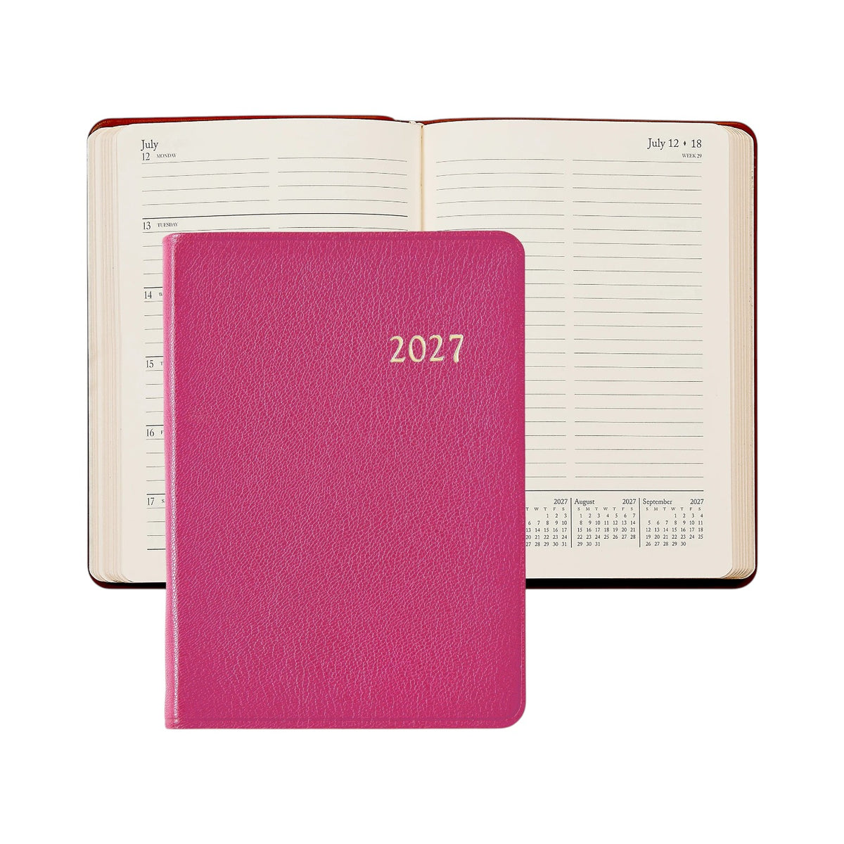 A pink Graphic Image 2027 Daily Journal closed, positioned in front of an open appointment book that displays a week in July and small yearly calendars at the bottom of the pages.