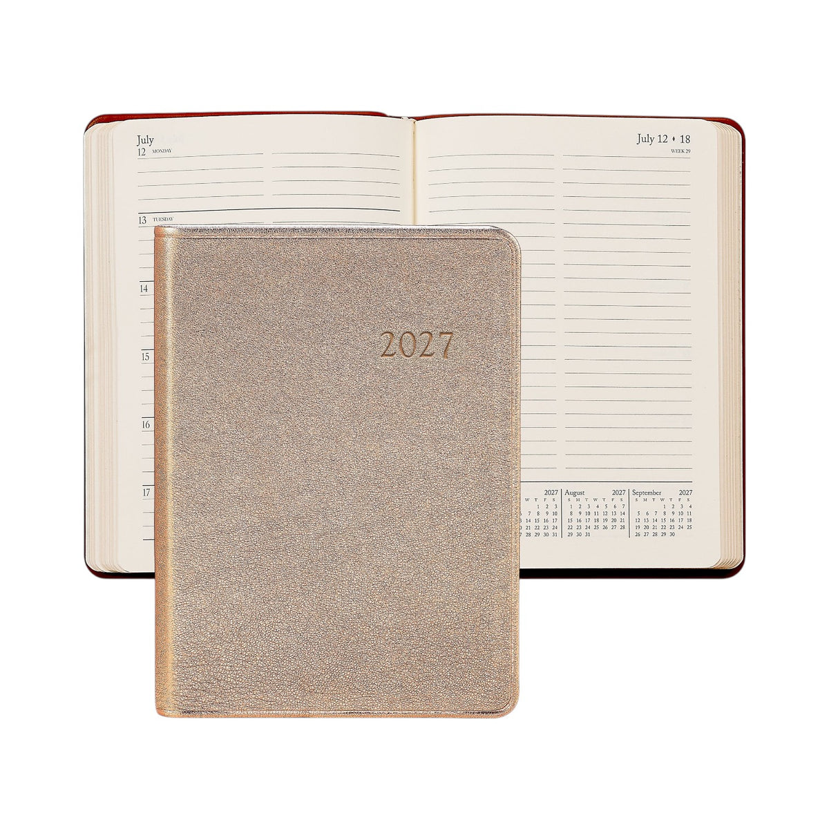 A closed Graphic Image 2027 Daily Journal with a metallic cover is displayed in front of an open appointment book that shows lined pages and a monthly calendar section.