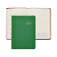A Graphic Image 2027 Daily Journal in green is closed and placed on top of an open diary showing a weekly layout for July 12–18.
