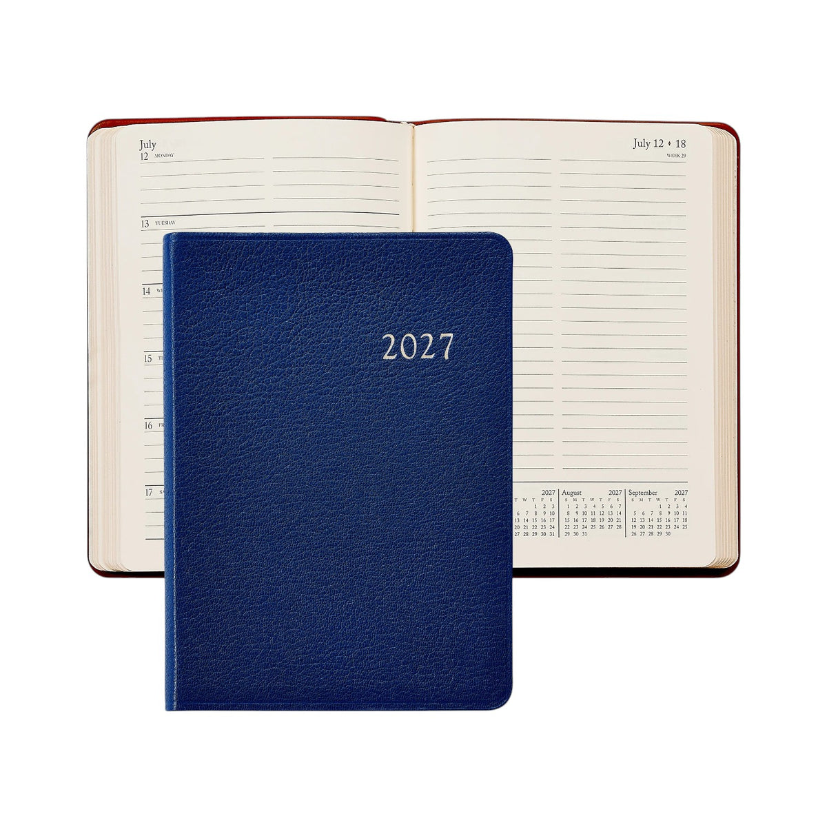 A closed Graphic Image 2027 Daily Journal in blue rests atop an open diary displaying a dated weekly layout alongside a small calendar.