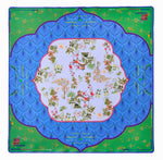 The Oh My Mahjong Mahjong Mat Collection features a square, non-slip mat with a blue scalloped pattern, green corners, and an Asian-inspired central design of trees, houses, and birds.