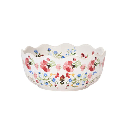 The Sofia Serveware Collection by Juliska features a white ceramic bowl with ruffled silhouette and scalloped edges, decorated in a vibrant floral motif of red, pink, green, and blue.