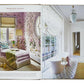 An open book, "**Decorate Like A Decorator**" from **Phaidon**, displays home interior design ideas with rooms featuring floral wall patterns, a pink armchair, a white bathtub near large windows, and various decor—all accompanied by expert decorating tips.