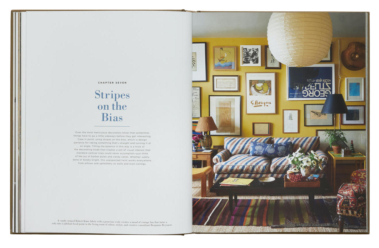 Open book showing Chapter Seven titled "Stripes on the Bias" from FREDERIC magazine. On the right page is a colorful living room with a striped sofa, various framed pictures on the yellow wall, and "Decorate Like A Decorator" by Phaidon showcasing clever designer tricks and decorating tips.