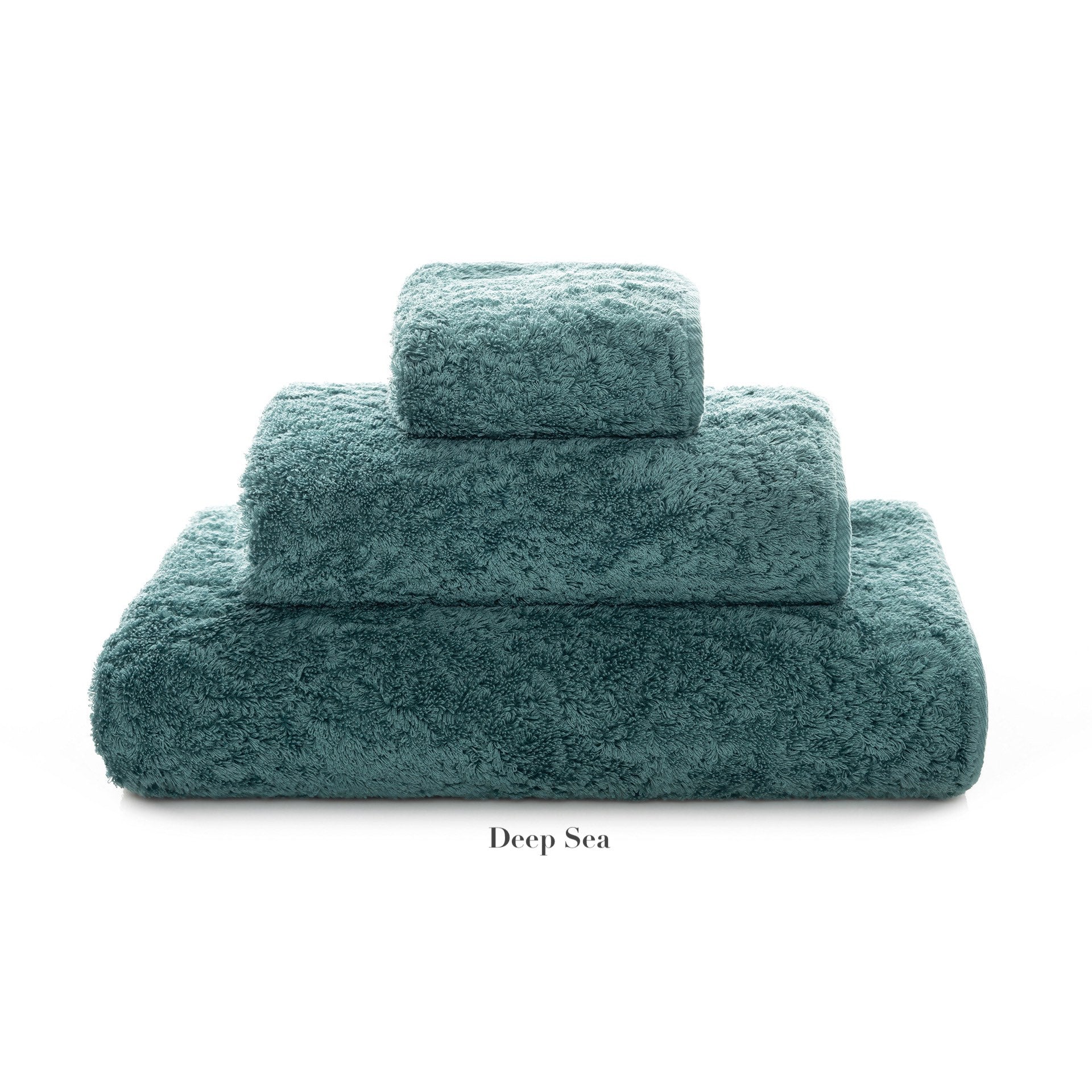 Three teal towels of different sizes, from Graccioza's Egoist Bath Collection, made of Egyptian cotton and stacked neatly, labeled "Deep Sea" against a white background.