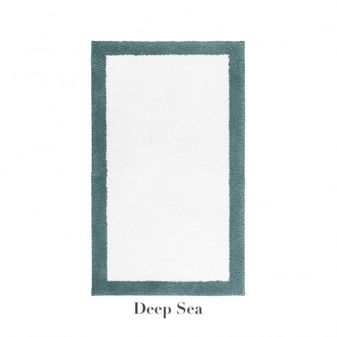 The Egoist Border Bath Rug by Graccioza is a rectangular white Egyptian cotton bath rug with a customizable thick teal border, non-slip silicone backing, and "Deep Sea" label below the image.
