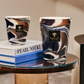 Two Baobab Collection Delta Nil Candles with a floral fragrance on a glass table with stacked books titled "Pearl Necklace French Riviera.