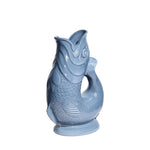 The Original Gluggle Jug’s Fish Gluggle Jug Collection features iconic ceramic fish-shaped pitchers in light blue with detailed scales and fins, standing upright—a true British design icon.