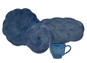 Four blue woven placemats from Juliska’s Le Panier Mystic Knot Denim Dinnerware and Serveware Collection, featuring intricate mystic knot designs, are displayed behind a matching blue Juliska mug adorned with a similar knot motif, evoking the artful elegance of a large charger or serving platter.