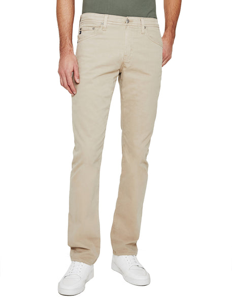 Man standing wearing AG Jeans Everett Sueded beige pants and white sneakers, view from mid-rise waist to feet.