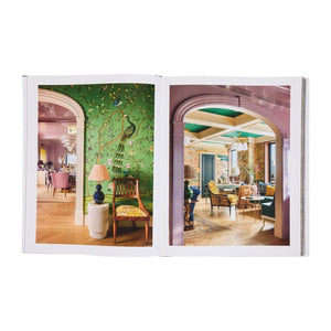The open "Design Reimagined" book by Rizzoli showcases colorful, ornately decorated rooms with patterned wallpaper and elegant furniture—perfect inspiration for glamorous home decor.