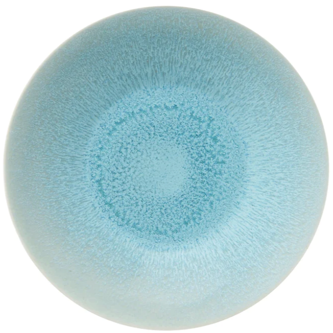 The Jars Vuelta Ocean Blue Collection features a round, light blue ceramic plate with a speckled ocean glaze gradient radiating from the center, adding timeless elegance to any table.