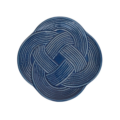 A round charger plate from the Juliska Le Panier Mystic Knot Denim Dinnerware and Serveware Collection, featuring a denim blue glaze and a white braided rope pattern in a symmetrical mystic knot design.