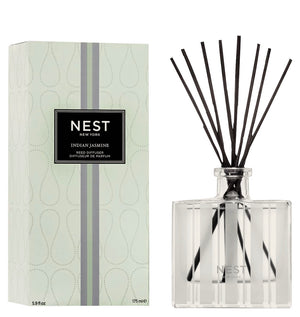 A bottle of Nest Indian Jasmine Reed Diffuser with black reeds is placed beside its patterned box, featuring notes of jasmine absolute and hints of red berries.
