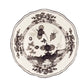 The Oriente Italiano Albus Dinnerware Collection from Ginori 1735 features a porcelain plate with black and white floral motifs and scalloped edges, inspired by elegant nature-themed Oriente Italiano design.