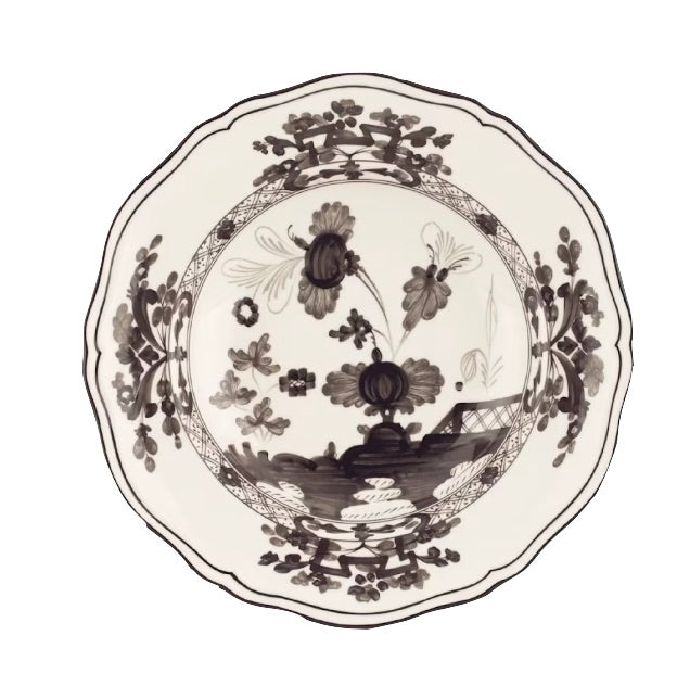 The Oriente Italiano Albus Dinnerware Collection from Ginori 1735 features a porcelain plate with black and white floral motifs and scalloped edges, inspired by elegant nature-themed Oriente Italiano design.