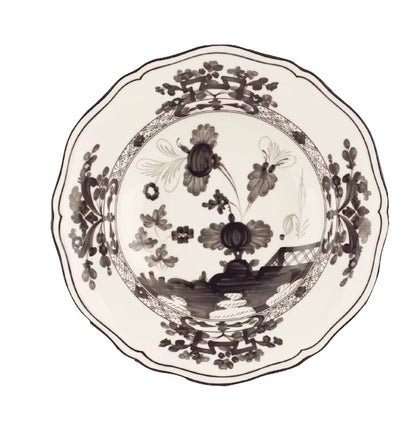 The Oriente Italiano Albus Dinnerware Collection from Ginori 1735 features a porcelain plate with black and white floral motifs and scalloped edges, inspired by elegant nature-themed Oriente Italiano design.