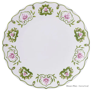A white dinner plate with green and pink floral patterns around the edge, intricately crafted from fine bone china by Royal Crown Derby. The words "Royal Crown Derby Cobblers Cove Camelot Collection" are elegantly printed at the bottom right, embodying the sophistication of a luxury boutique hotel.