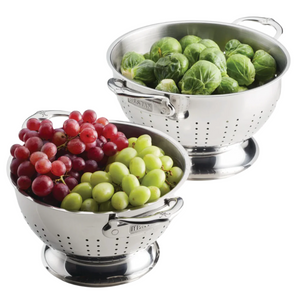 The Hestan Provisions Stainless Steel Colander 2-Piece Set sits side by side—one filled with grapes, the other with Brussels sprouts—providing superior drainage and ergonomic handles for effortless rinsing.