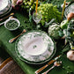 The Albertine Collection by Bernardaud, with its scalloped-edge plates, silver cutlery, candles, wine glasses, peas, and fresh vegetables on a green tablecloth, creates a poetic green-themed table decor.