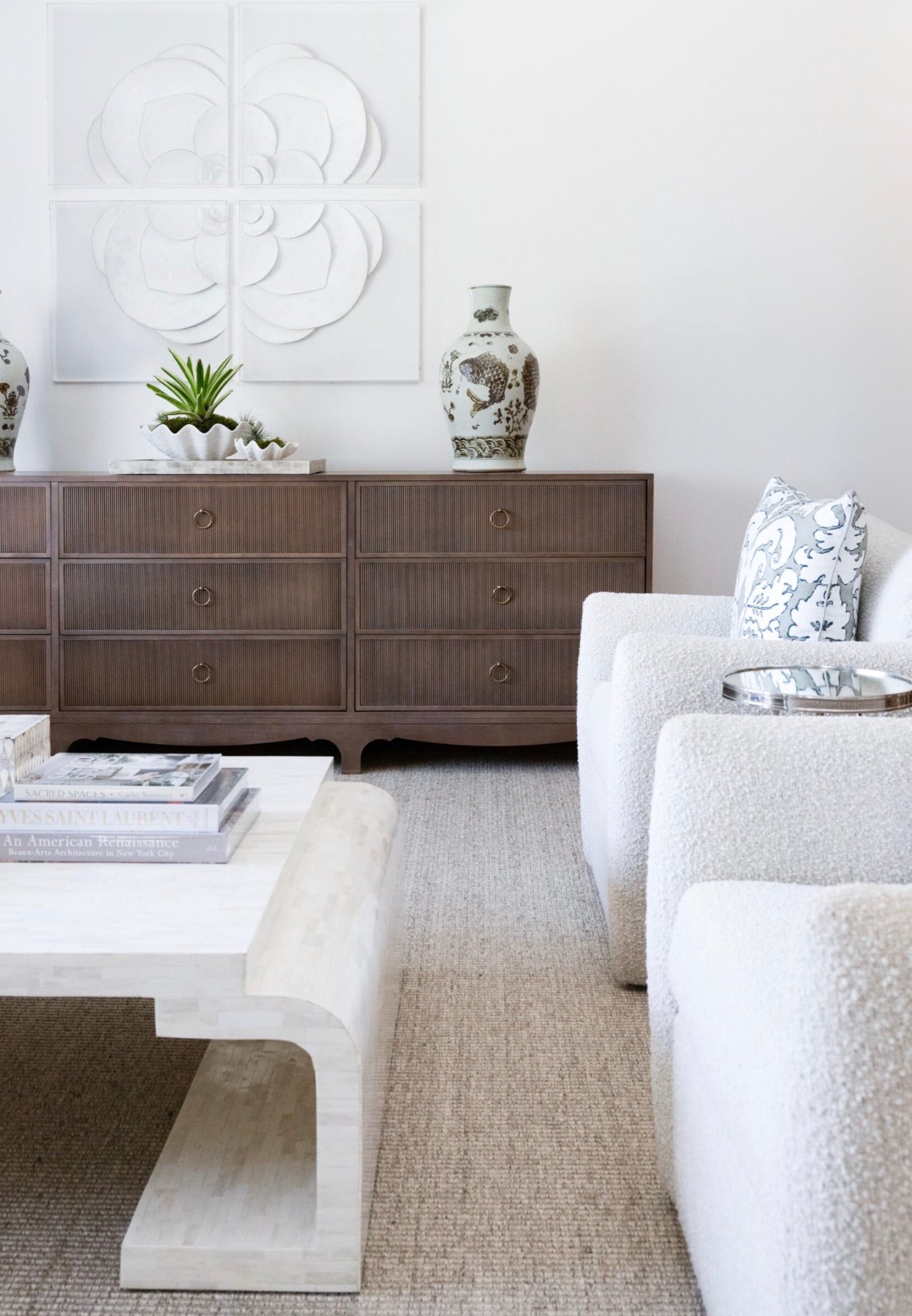 A modern living room features a white coffee table, a Century Furniture Reeded Dresser with reeded case front and charcoal finish, decorative vases, white armchairs, and a large floral wall art piece.