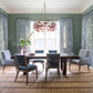 A dining room featuring the Hickory Chair Oliver Extension Dining Table with six gray chairs, a woven rug, blue patterned curtains, a pink chandelier, and a vase of greenery as the centerpiece.