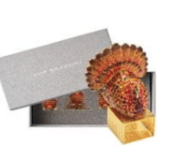 A beaded Turkey Trot Napkin Ring on a gold-tone band, with a set of identical napkin rings for Thanksgiving table settings in a gray box behind it.