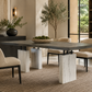 Modern dining room with the Block Dining Table by Hickory Chair—a rectangular minimalist piece featuring striking marble legs—paired with four upholstered chairs, a decorative bowl of moss, a large plant, and neutral-toned decor.