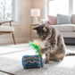 A gray tabby cat plays with the Meowwife Sardines Cat Toy by Haute Diggity Dog, which features blue coloring and green and yellow feather toppers, on a light-colored rug in the living room, enjoying the enticing scent of organic catnip inside this high-quality toy.
